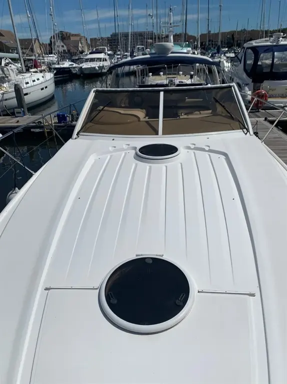 A view from above a white boat's deck, featuring portholes, with multiple boats docked at a marina in the background.